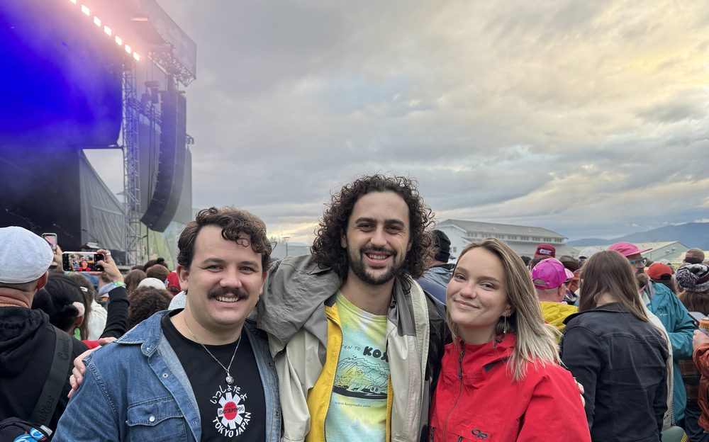 Three attendees at Zootown Music Festival in Missoula Montana with stage lights and cloudy sky